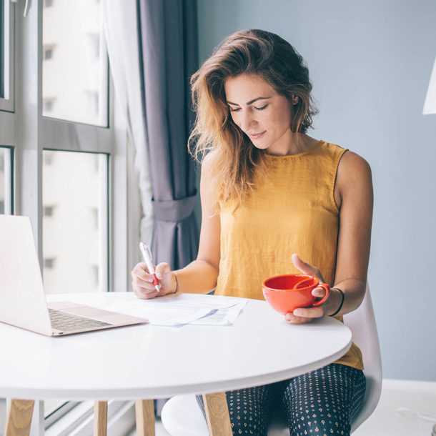 Focused female sitting at table with notebook and cup filling documents