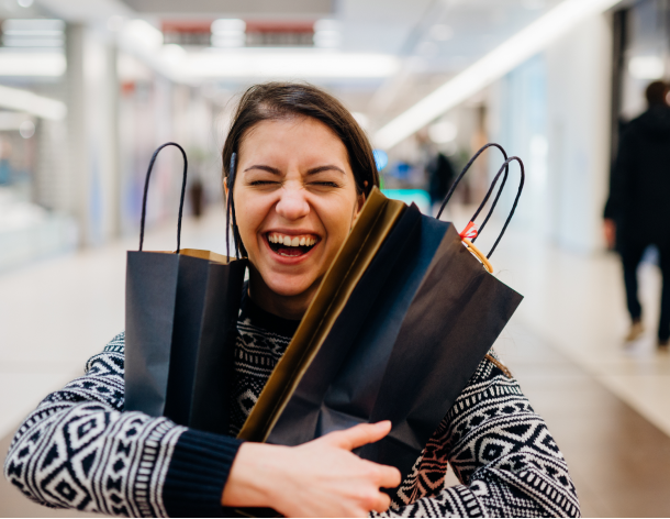 Smiling girl hugs two shopping bags in a mall.