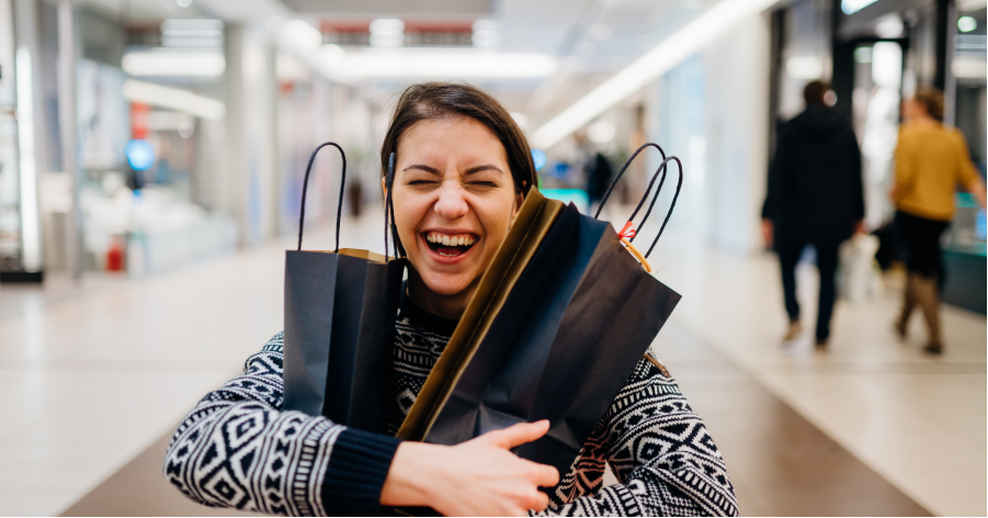 Smiling girl hugs two shopping bags in a mall.