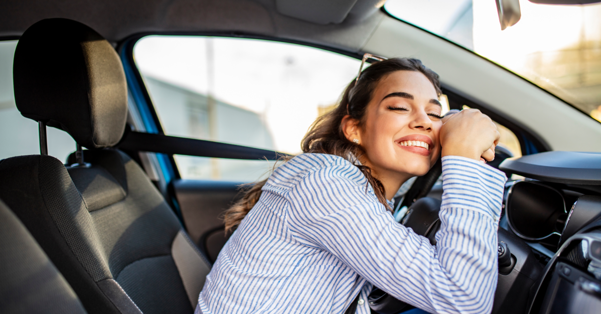 Girl smiling while holding steering wheel in her car.