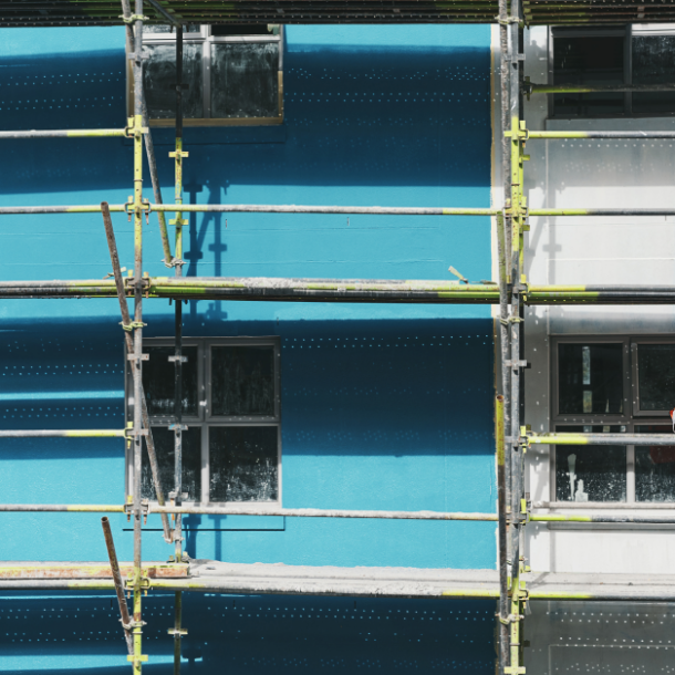 Two construction employees stand on scaffolding.