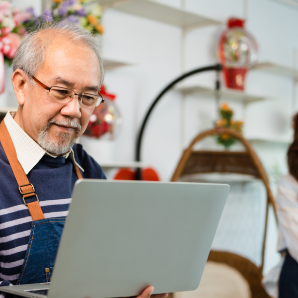 Man wearing an apron holds a laptop in a flower shop.