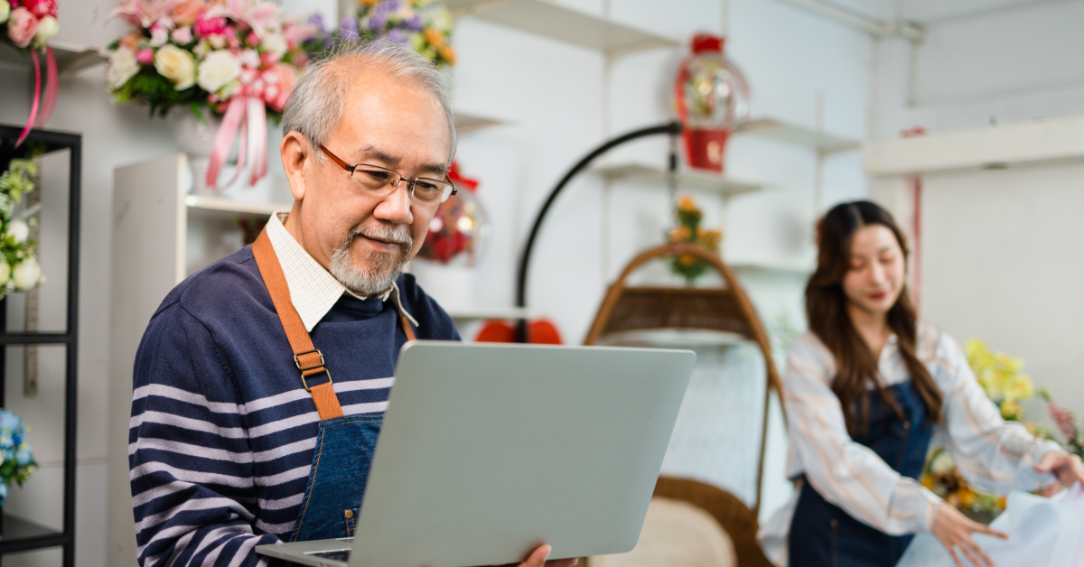 Man wearing an apron holds a laptop in a flower shop.