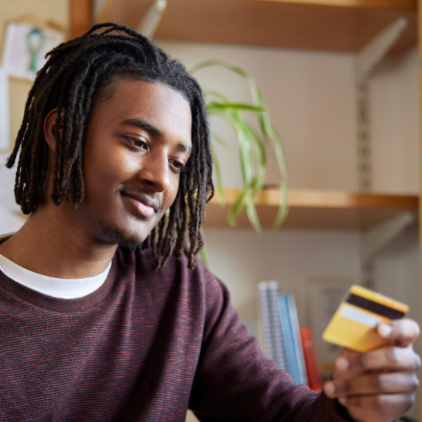 Young man in a dorm room holds a credit card