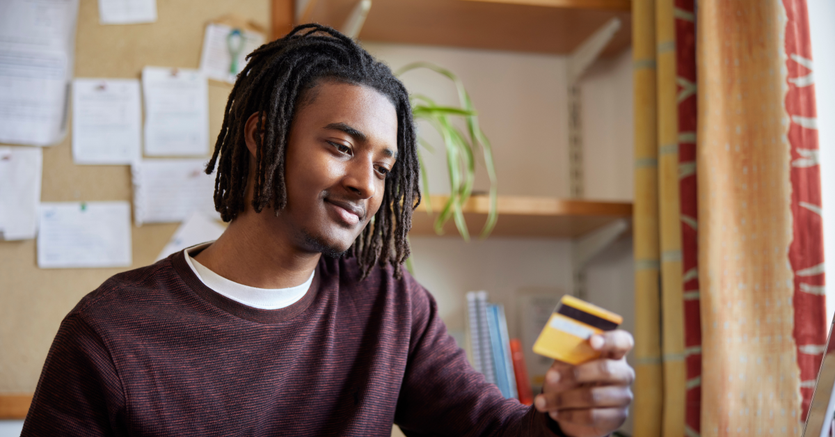 Young man in a dorm room holds a credit card