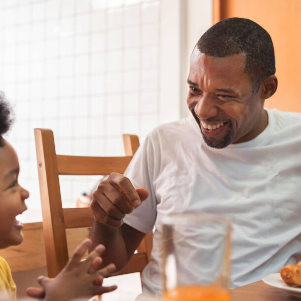 Dad and child laugh while eating breakfast.