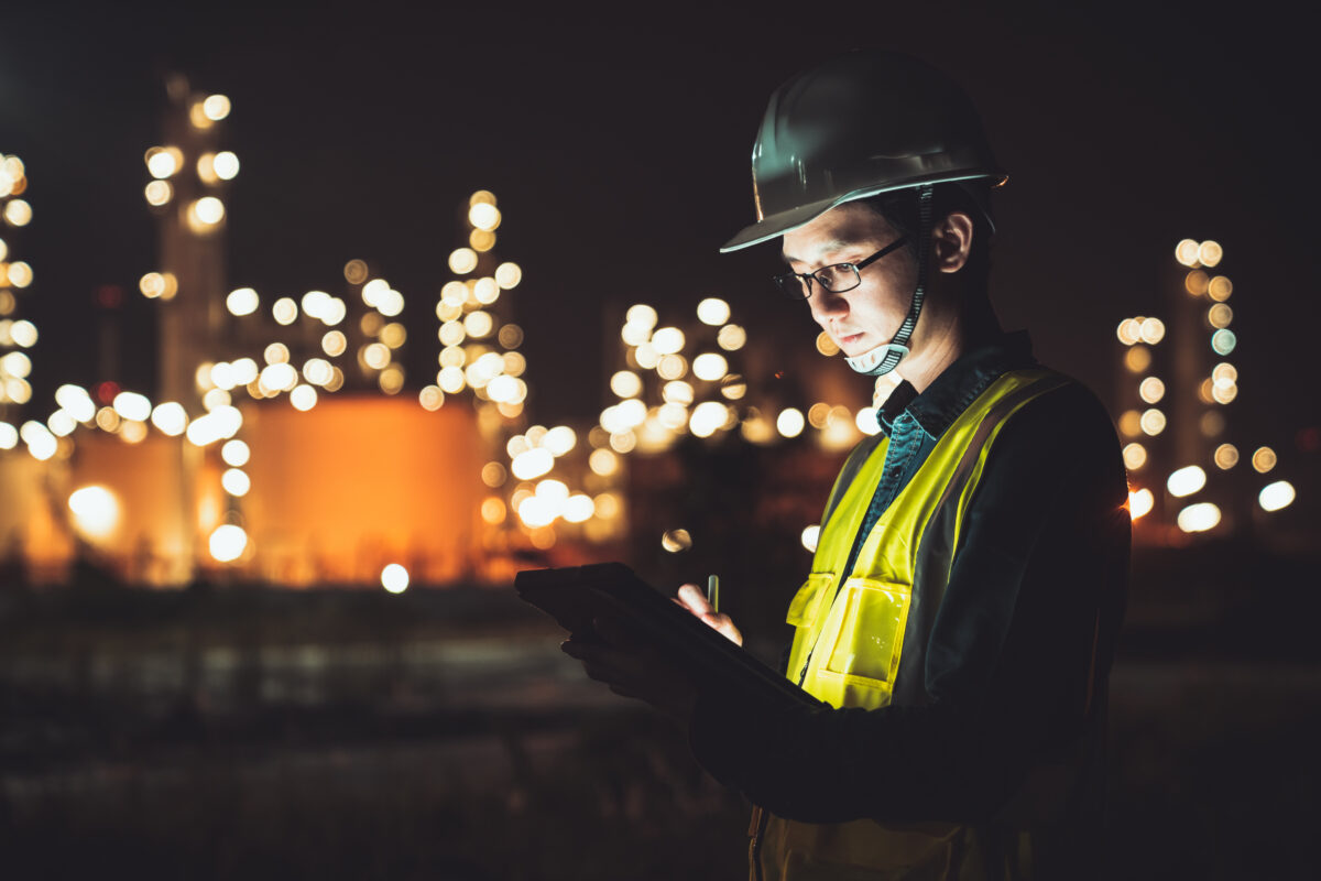 An employee wearing a yellow vest is looking at his clipboard, during a night shift.