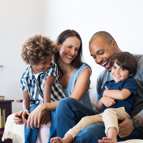 Two parents and their 2 young children sitting on the sofa and laughing with each other.