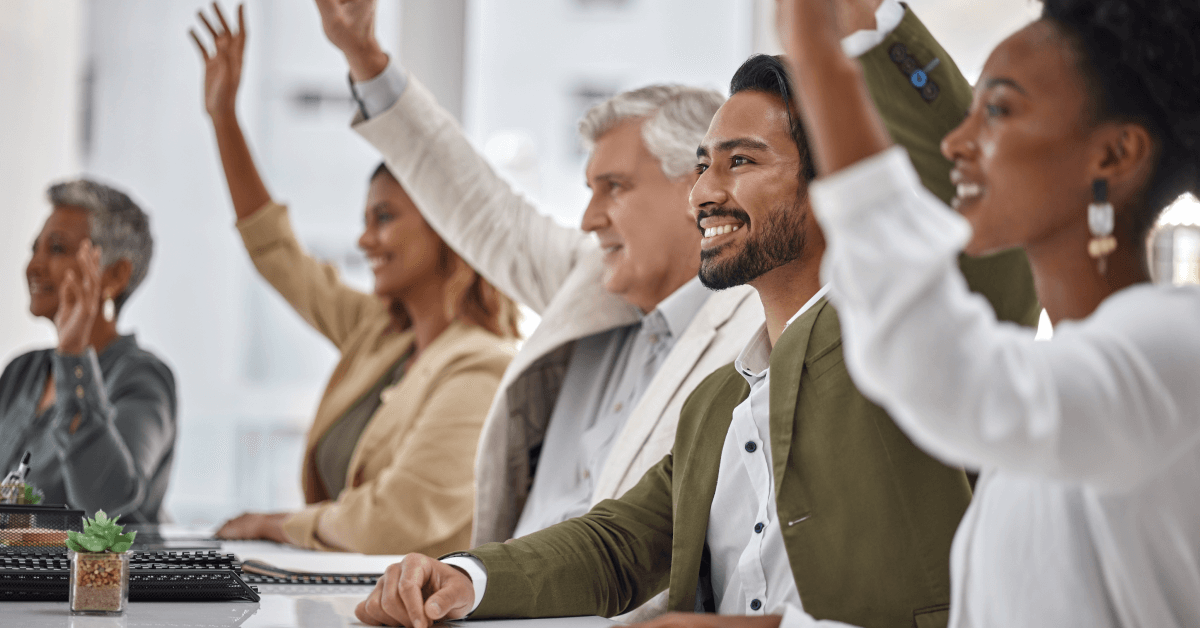 5 employees sitting at a table. 3 are raising their hands.